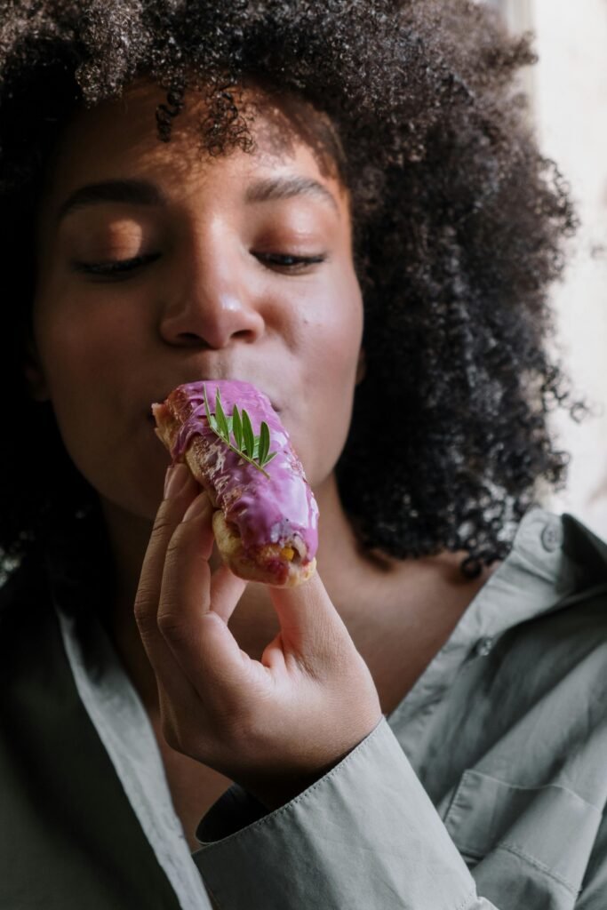 Close-up of a woman savoring a delightful purple glazed eclair indoors.